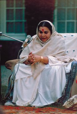 Shri Mataji Nirmala Devi sitting outside, white sari & grey shawl
