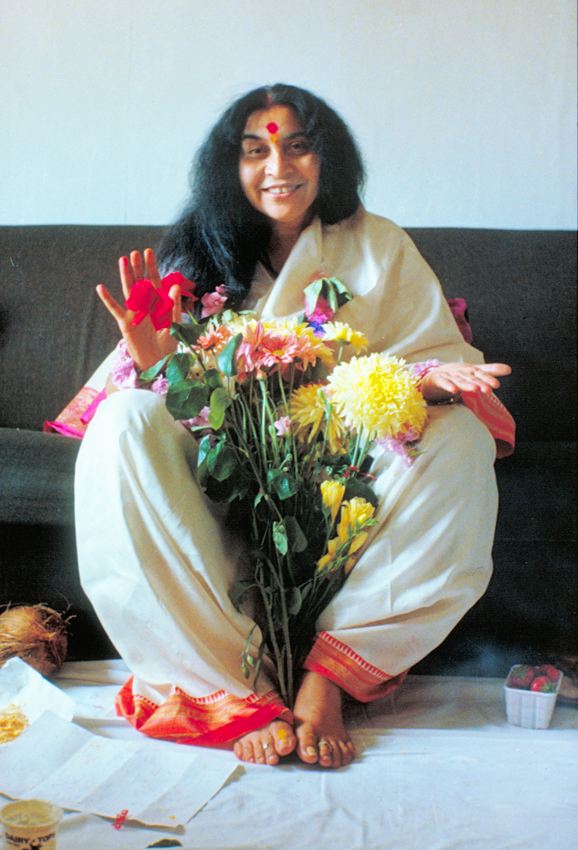Shri Mataji sitting with flowers on a sofa in the United Kingdom